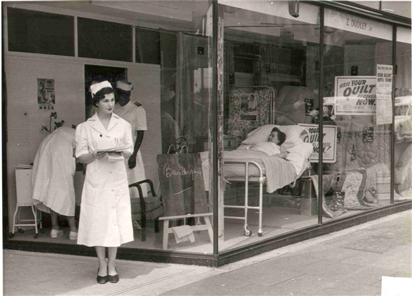 Photo:A NHS reservist nurse with leaflet standing outside the Clapton Electricity Showrooms, on Lower Clapton Road. A window display with a lady lying in bed can be seen, Apr 1955 (Catalogue reference: SBHH-PG-188).